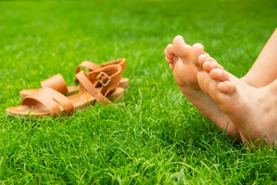 Photo of Woman resting barefoot near sandals on green grass outdoors, closeup