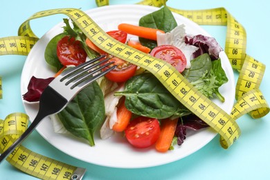 Photo of Measuring tape, vegetable salad and fork on light blue background, closeup. Weight loss concept