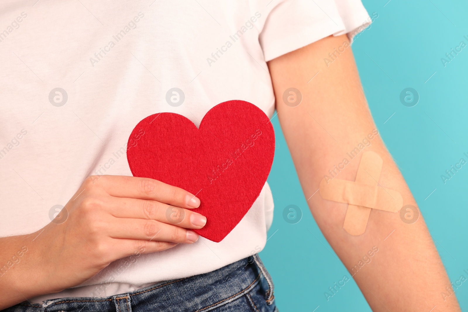 Photo of Woman holding heart near hand with adhesive plasters against color background, closeup. Blood donation