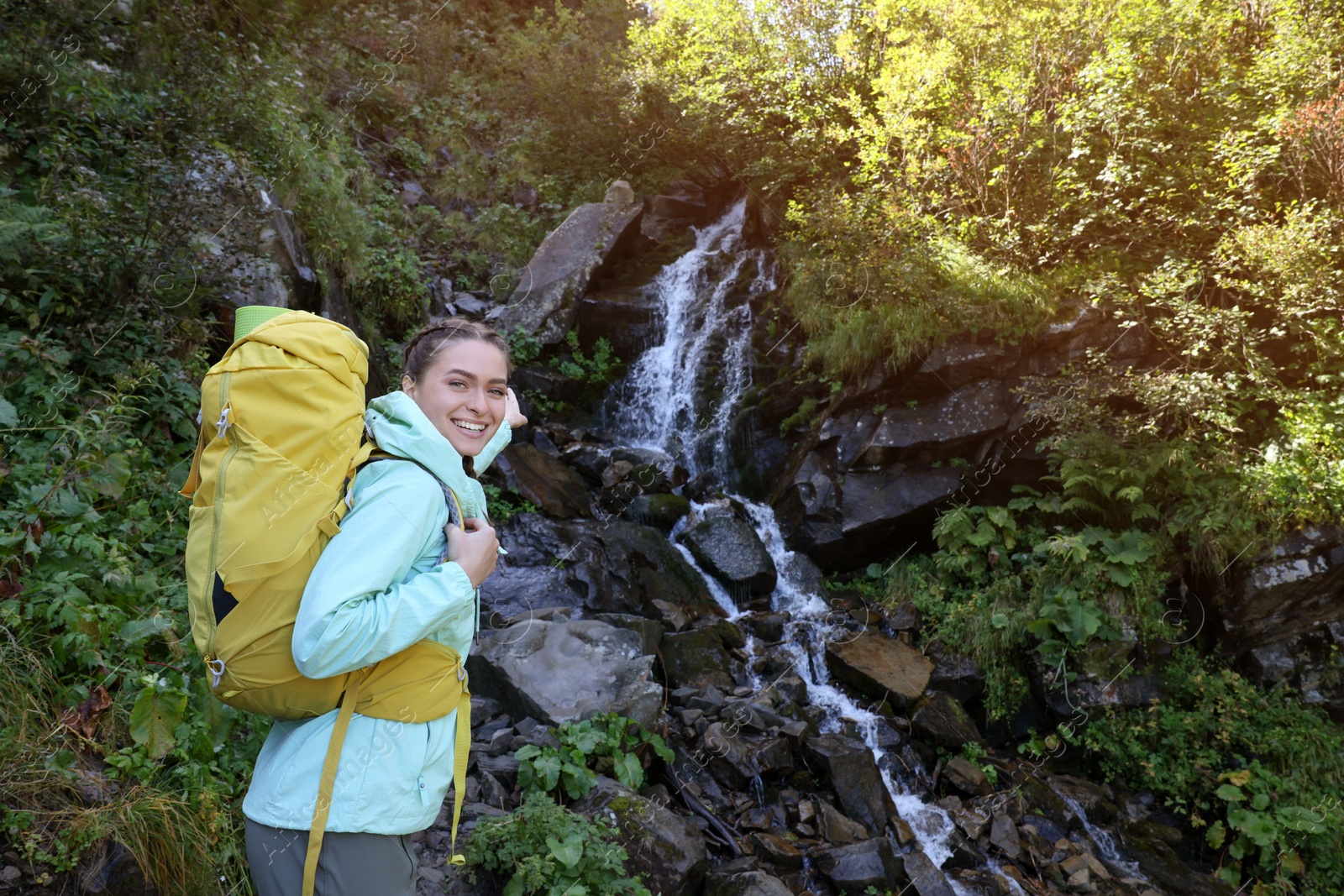 Photo of Tourist with backpack near waterfall in mountains. Space for text