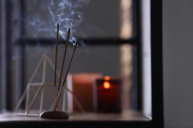 Photo of Incense sticks smoldering on shelf indoors, space for text