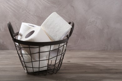 Photo of Soft toilet paper rolls in metal basket on wooden table, closeup. Space for text