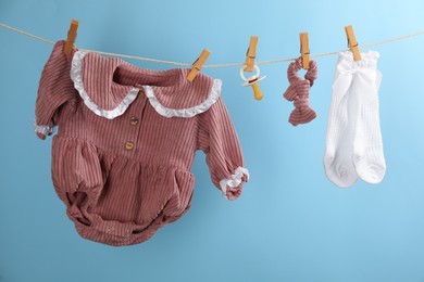 Photo of Baby clothes and accessories hanging on washing line against light blue background