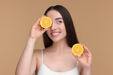 Beautiful young woman with pieces of orange on beige background