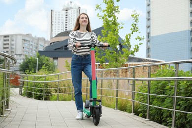 Photo of Happy woman with modern electric kick scooter on city street
