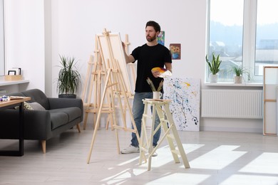 Photo of Man painting in studio. Using easel to hold canvas