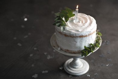 Photo of Tasty Birthday cake with burning candle and eucalyptus branches on grey table, space for text