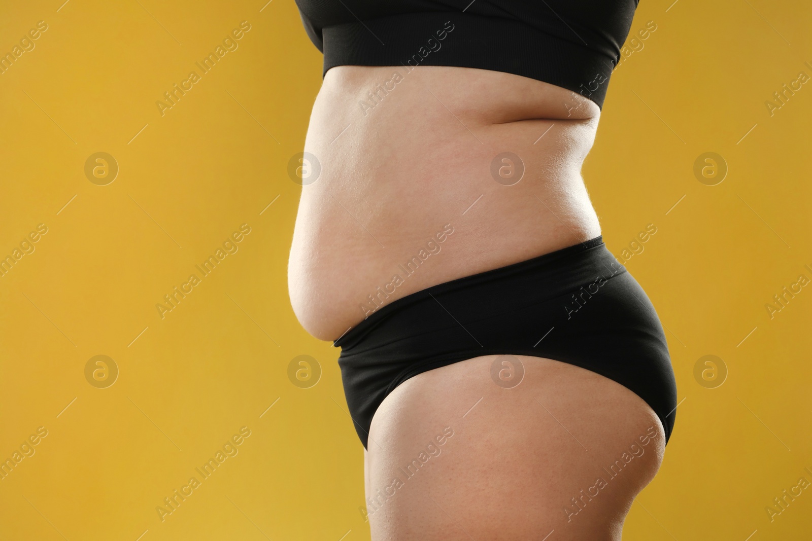 Photo of Woman with excessive belly fat on goldenrod background, closeup. Overweight problem