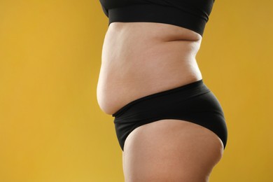 Woman with excessive belly fat on goldenrod background, closeup. Overweight problem