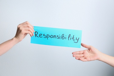 Woman giving light blue paper sheet with word Responsibility to colleague on white background, closeup