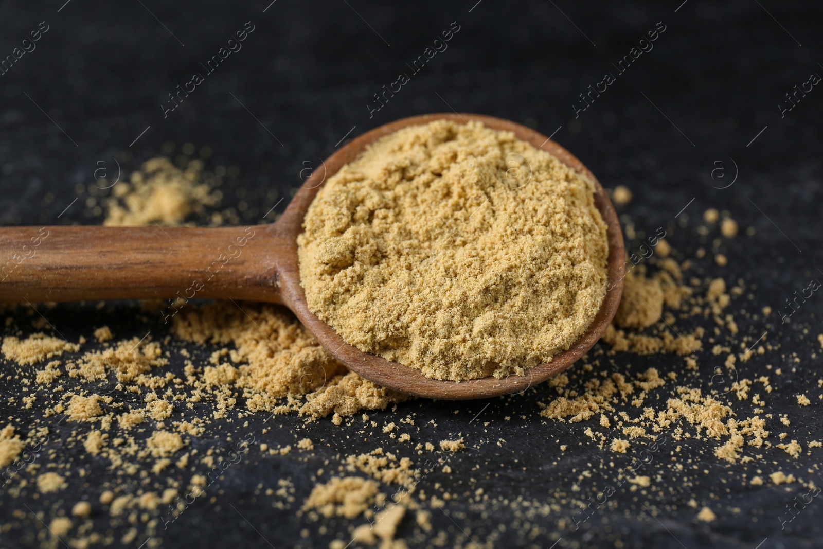 Photo of Wooden spoon of aromatic mustard powder on black table, closeup