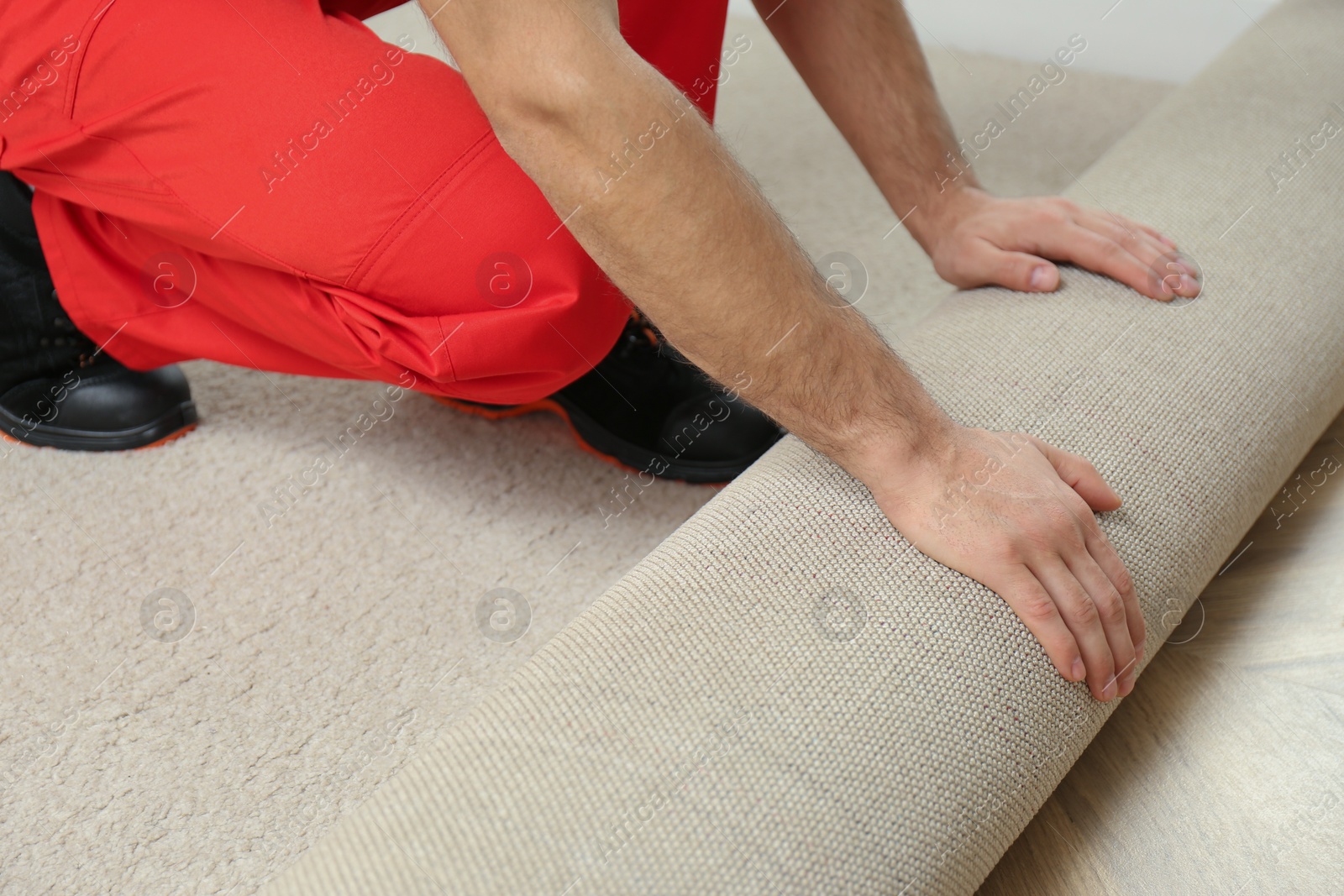 Photo of Worker rolling out new carpet flooring indoors, closeup