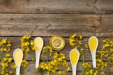Photo of Rapeseed oil in bowl, gravy boats and beautiful yellow flowers on wooden table, flat lay. Space for text