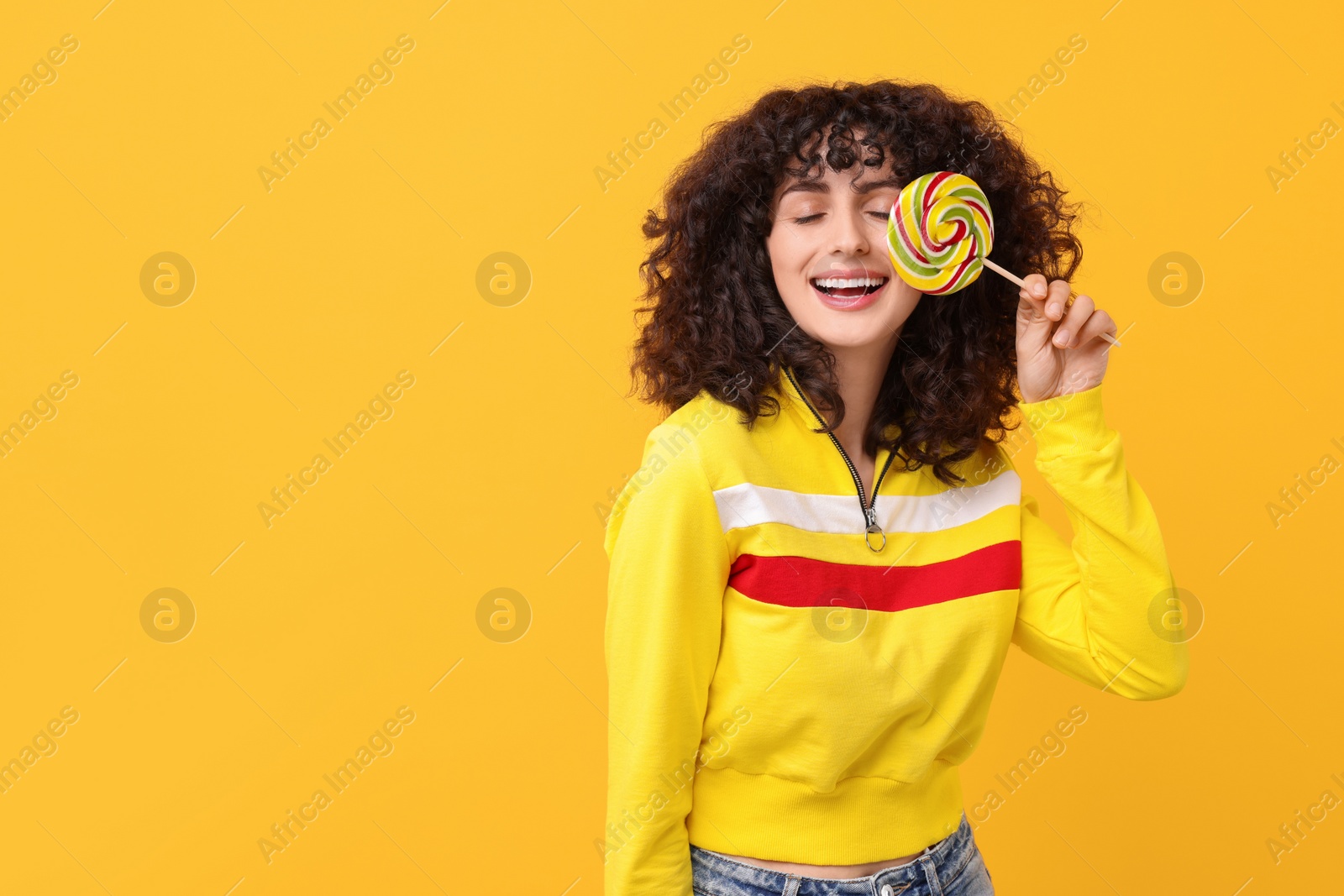 Photo of Beautiful woman covering eye with lollipop on yellow background, space for text