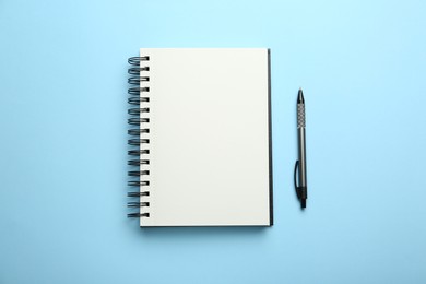 Notebook and pen on light blue background, top view