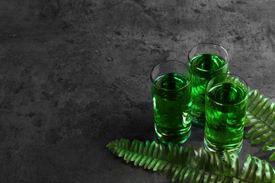 Photo of Absinthe in shot glasses and fern leaves on gray table, space for text. Alcoholic drink