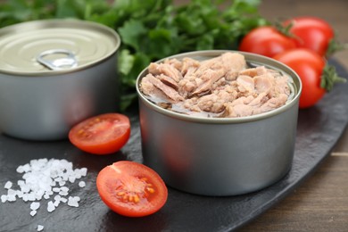 Tin cans with canned tuna, salt and tomatoes on wooden table, closeup