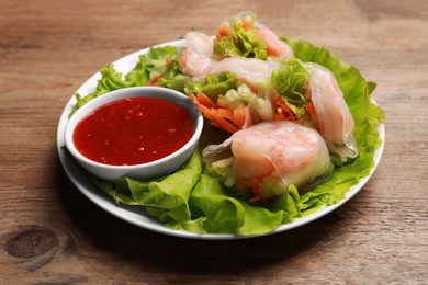 Photo of Tasty spring rolls served with lettuce and sauce on wooden table, closeup