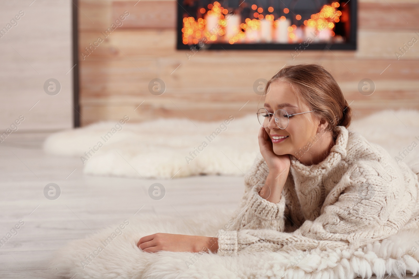 Photo of Beautiful young woman on rug at home, space for text. Winter atmosphere