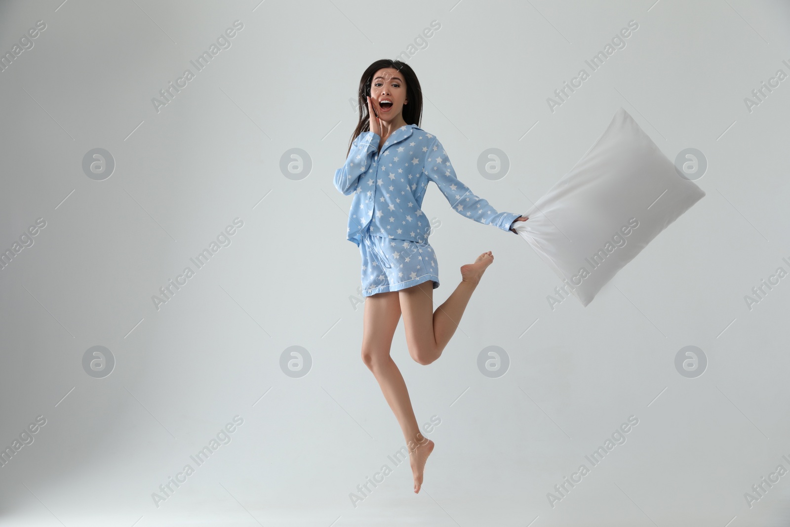 Photo of Beautiful Asian woman with pillow jumping on light grey background. Bedtime