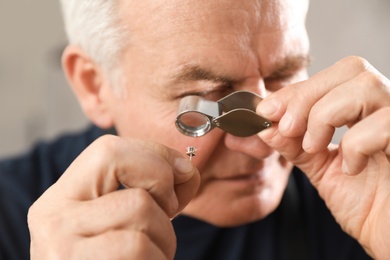 Photo of Male jeweler evaluating earring in workshop, closeup