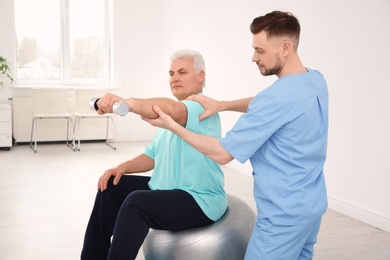 Photo of Young physiotherapist working with senior patient in clinic