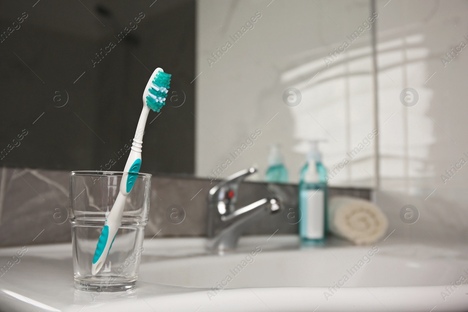 Photo of Light blue toothbrush in glass holder on washbasin