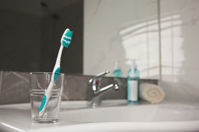 Photo of Light blue toothbrush in glass holder on washbasin