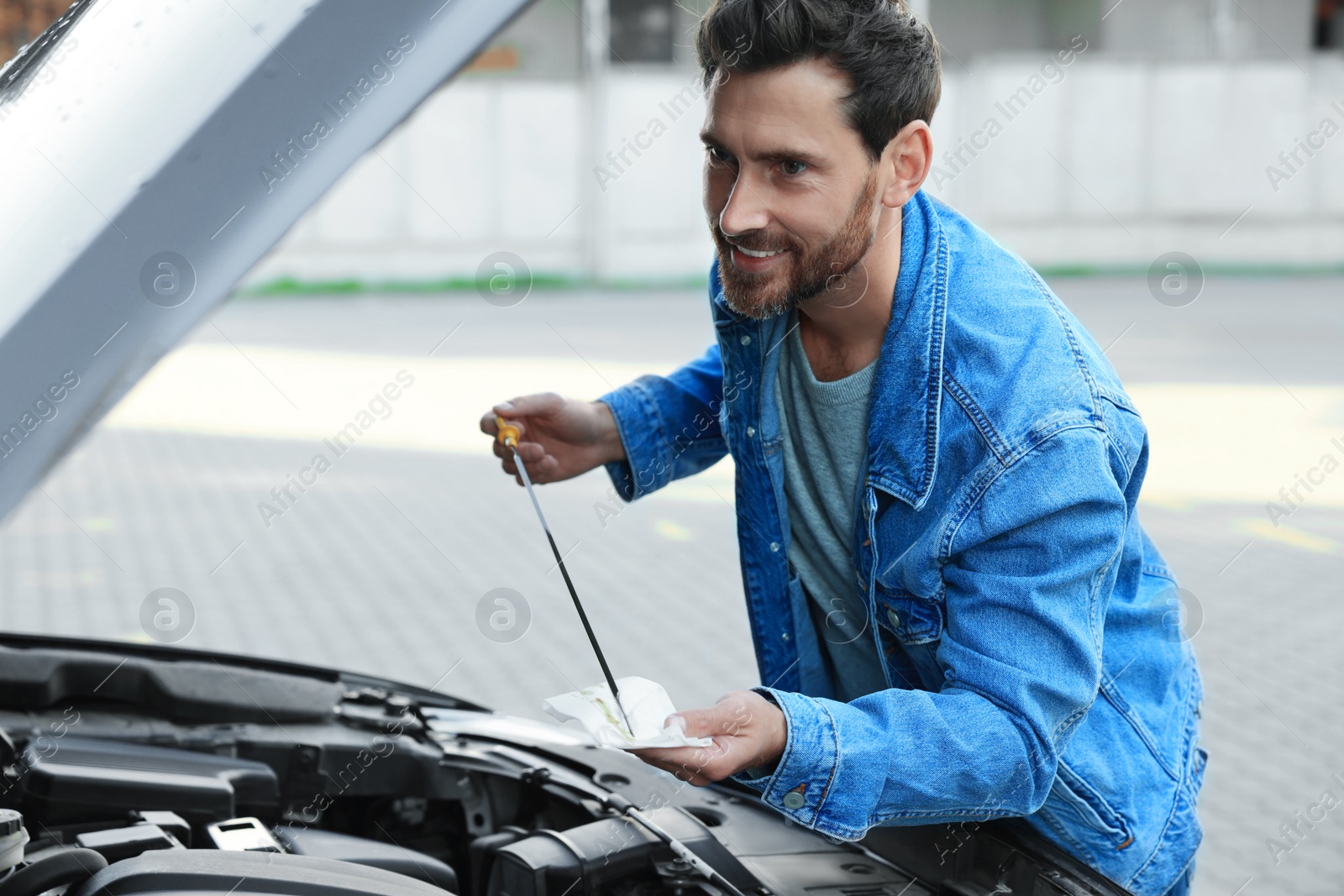 Photo of Man checking motor oil level with dipstick outdoors