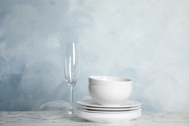 Photo of Clean plates, bowls and glasses on white marble table against light blue background. Space for text