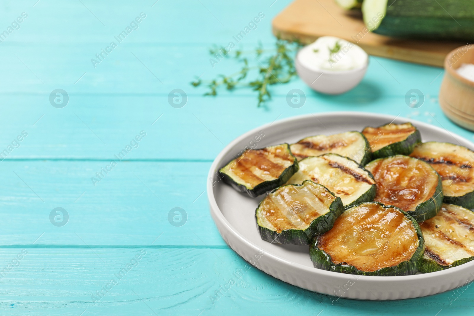 Photo of Plate of delicious grilled zucchini slices on light blue wooden table. Space for text