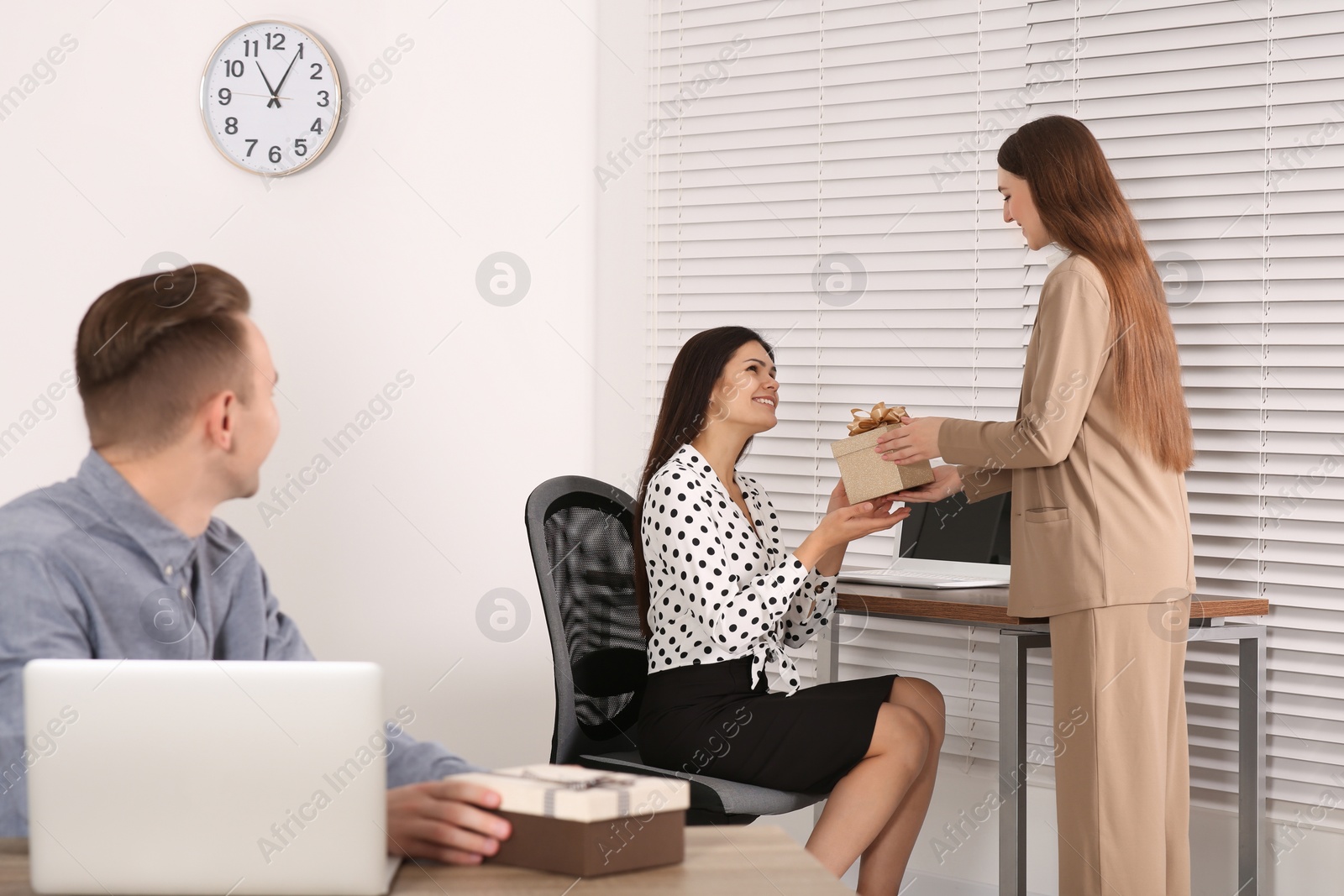 Photo of Woman presenting gift to her colleague in office