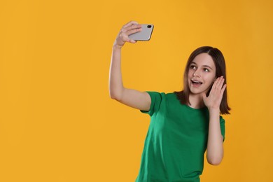 Photo of Teenage girl taking selfie on orange background. Space for text