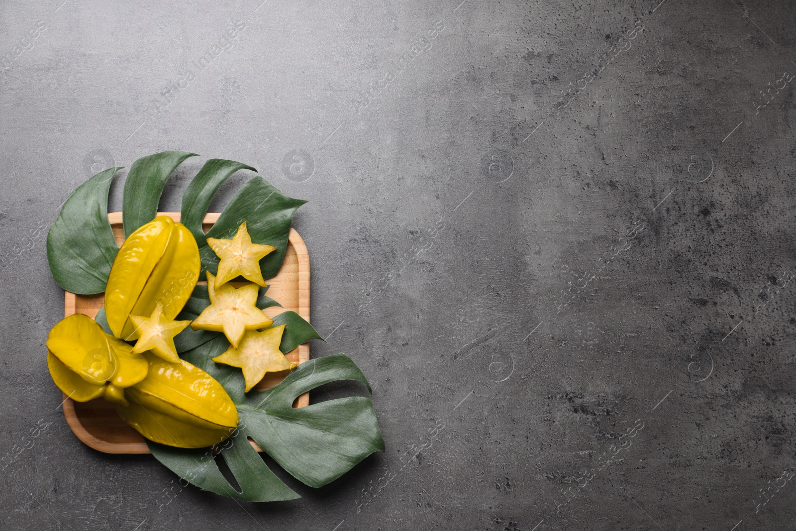 Photo of Delicious carambola fruits and green leaves on grey table, flat lay. Space for text