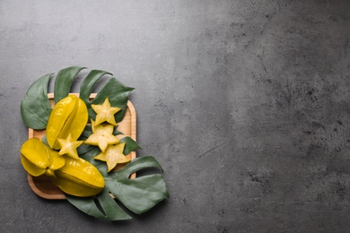 Photo of Delicious carambola fruits and green leaves on grey table, flat lay. Space for text