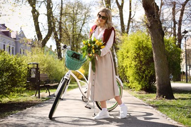 Beautiful woman with bouquet of yellow tulips and bicycle outdoors on sunny spring day