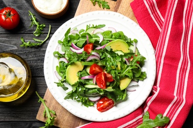 Photo of Delicious salad with avocado, arugula and tomatoes on black wooden table, flat lay