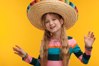 Photo of Cute girl in Mexican sombrero hat on orange background