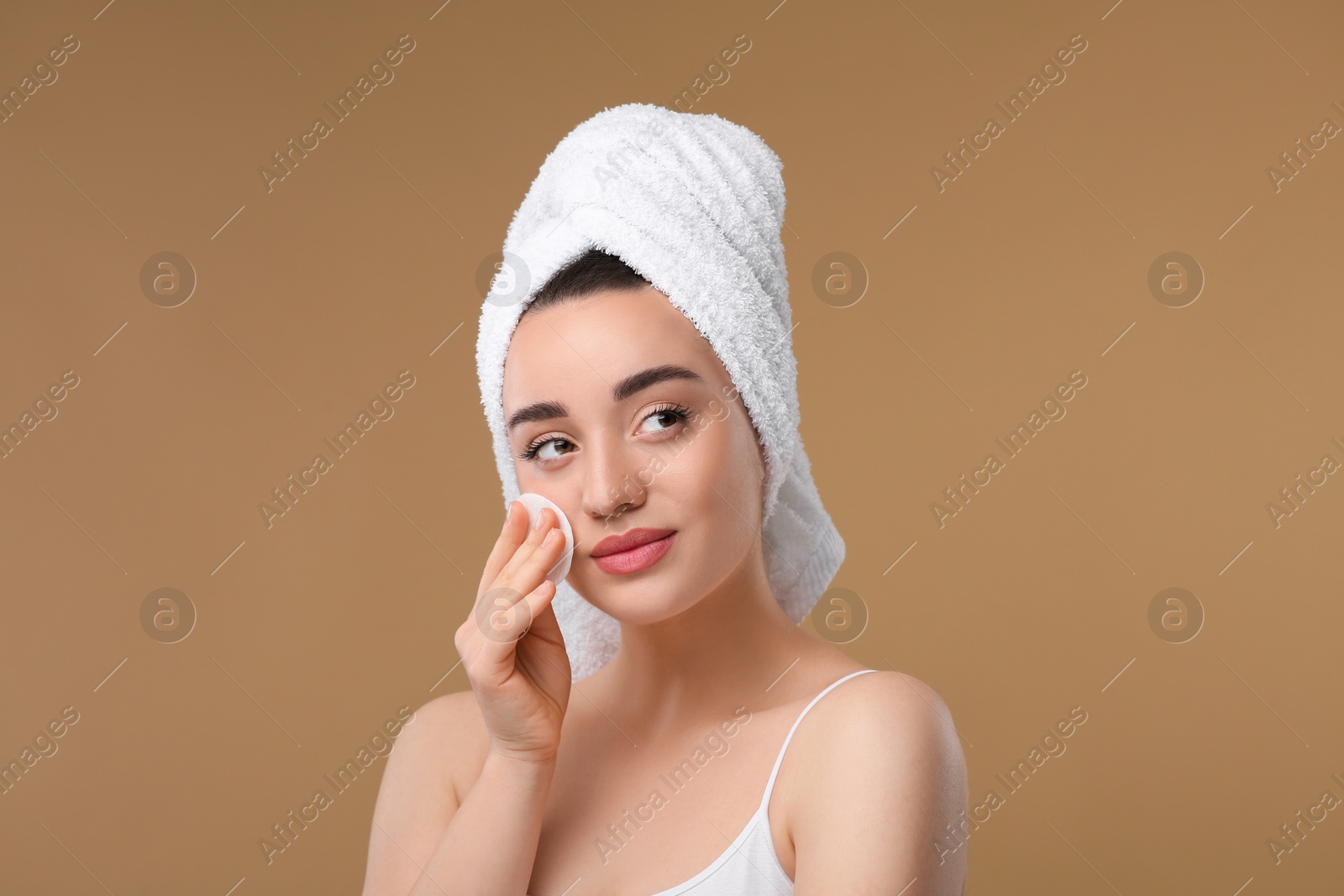 Photo of Beautiful woman in terry towel removing makeup with cotton pad on beige background