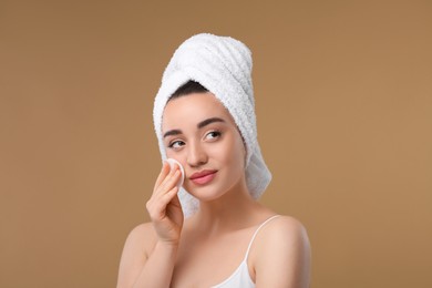 Beautiful woman in terry towel removing makeup with cotton pad on beige background