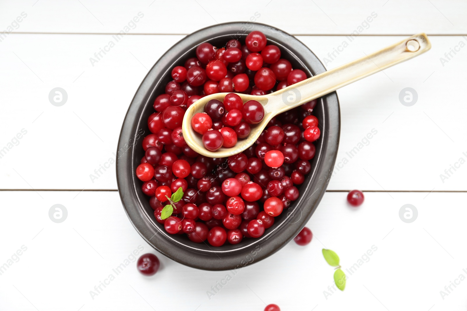 Photo of Fresh ripe cranberries in bowl and spoon on white wooden table, top view