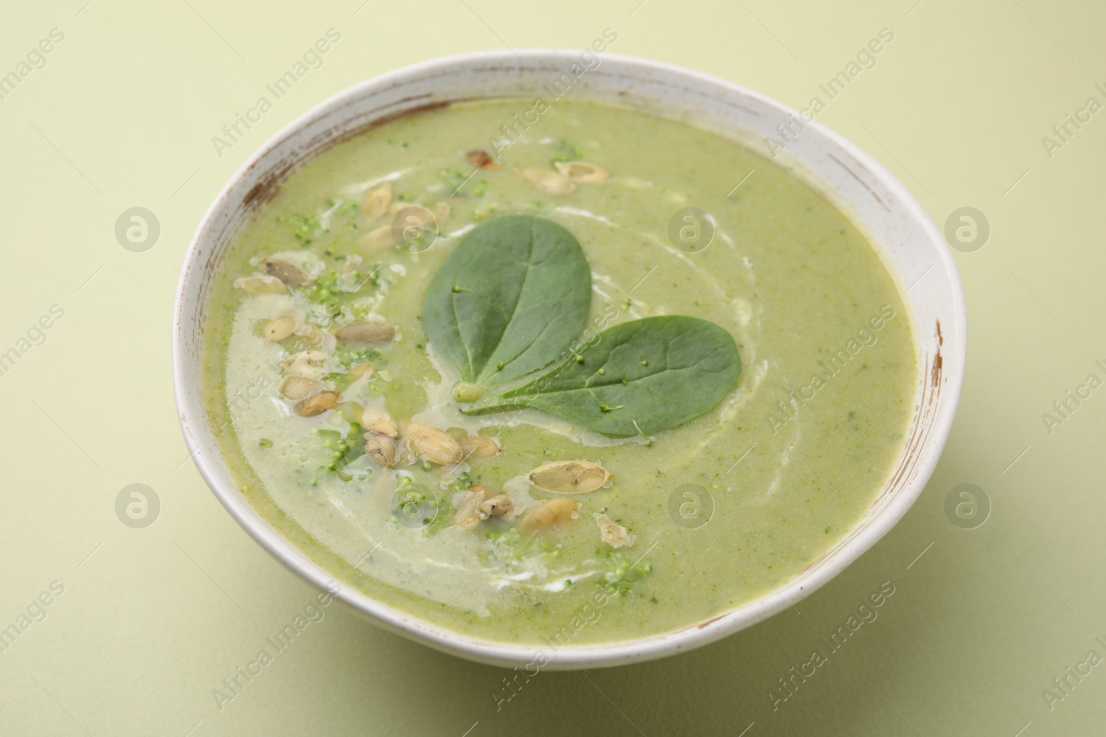 Photo of Delicious broccoli cream soup with basil and pumpkin seeds on green background, closeup