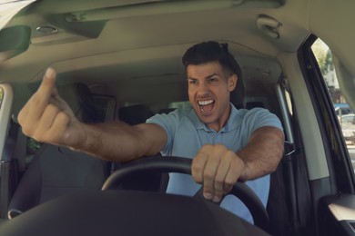 Photo of Stressed angry man showing middle finger in modern car, view through windshield
