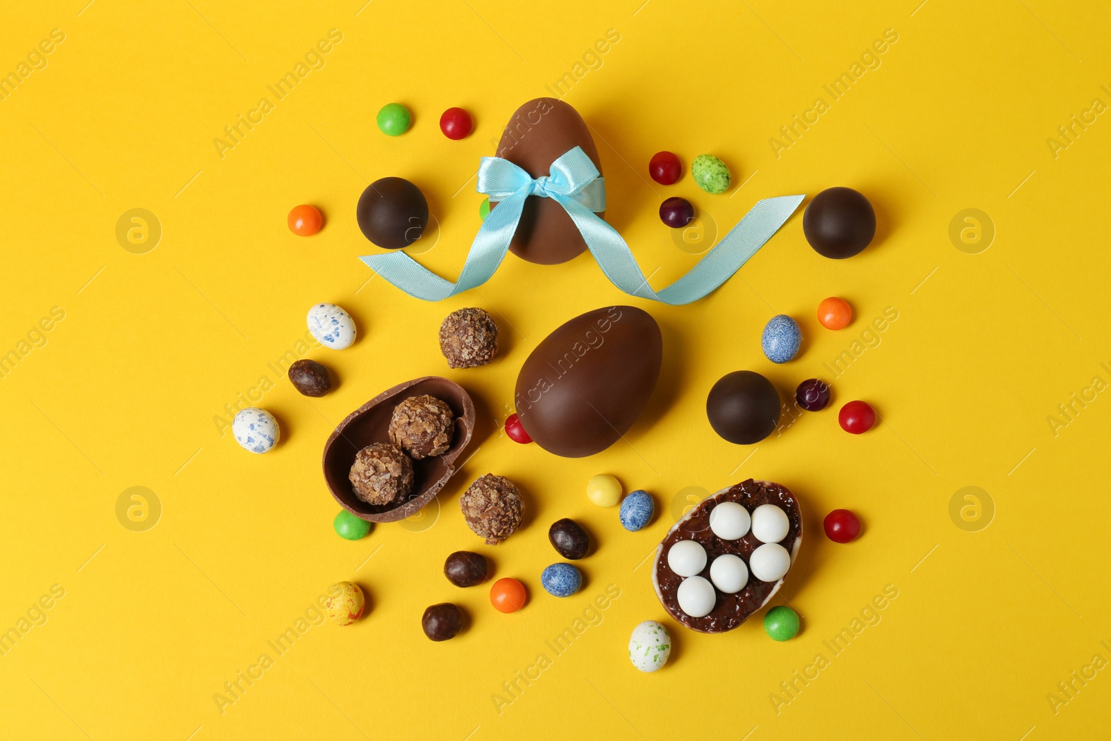 Photo of Tasty chocolate eggs and candies on yellow background, flat lay