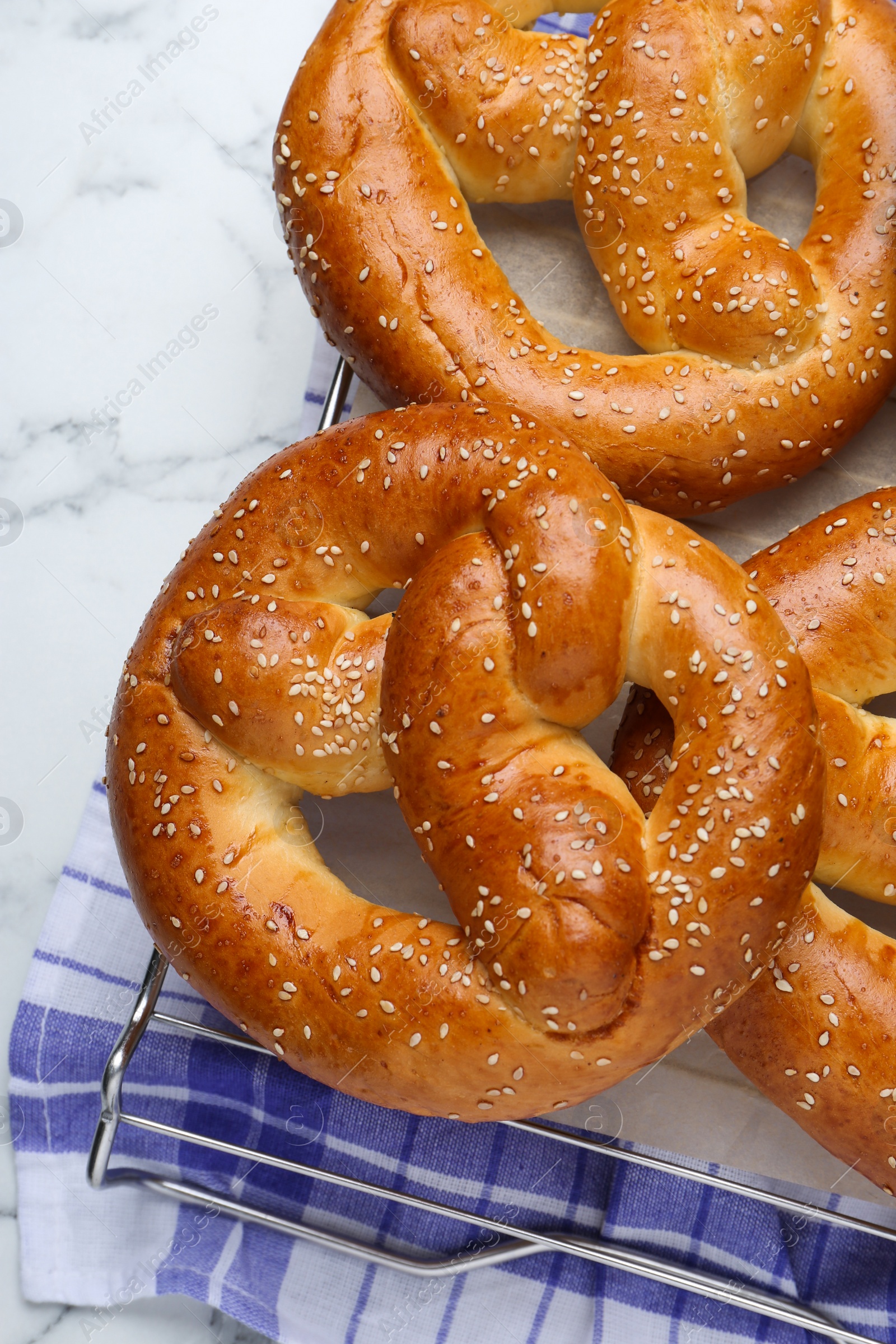 Photo of Cooling rack with delicious freshly baked pretzels on white marble table, top view