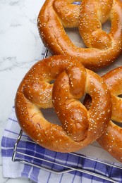 Cooling rack with delicious freshly baked pretzels on white marble table, top view