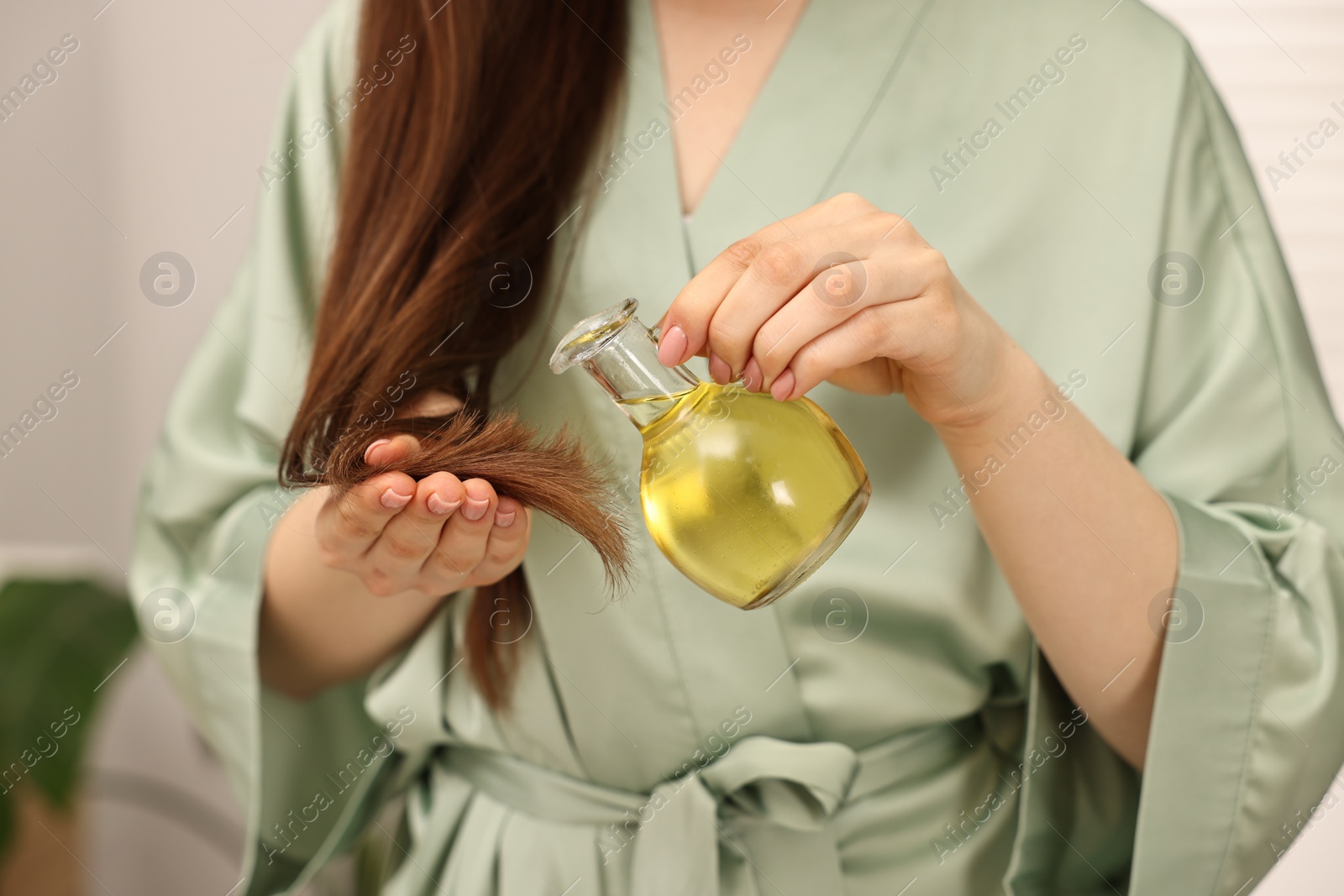 Photo of Woman applying oil hair mask onto ends at home, closeup