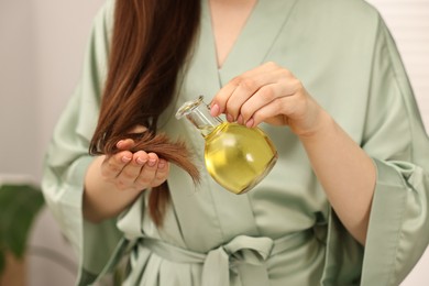 Photo of Woman applying oil hair mask onto ends at home, closeup