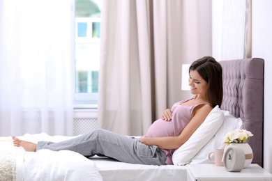 Happy pregnant woman lying on bed at home