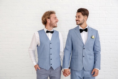 Photo of Happy newlywed gay couple in suits against white wall